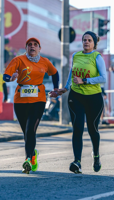 Atleta com deficiência visual e guia voluntária da Radar DV correm lado a lado durante prova de rua, demonstrando parceria, confiança e superação.