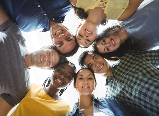 Grupo diverso de voluntários reunidos em círculo sorrindo para a câmera, simbolizando união, inclusão e trabalho em equipe.