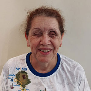 Maria, deficiente visual, secretária da Radar DV, sorrindo, vestindo camiseta branca com mapa ilustrado do Brasil.